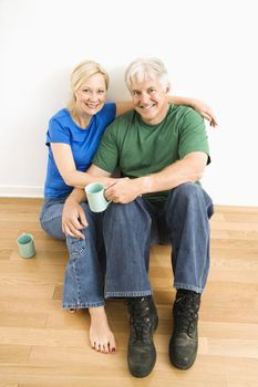 Middle-aged couple sitting on floor together drinking coffee.