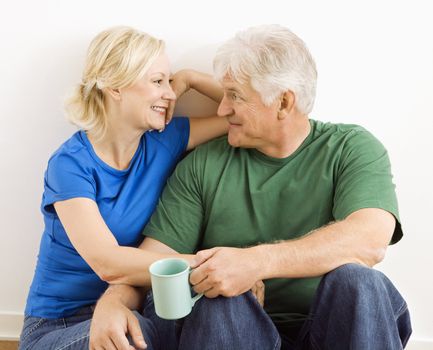 Middle-aged couple sitting together snuggling and drinking coffee.
