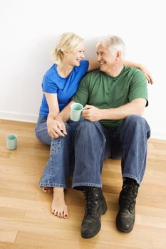 Middle-aged couple sitting on floor snuggling and drinking coffee.