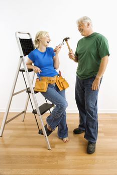 Middle-aged couple with household tools next to ladder.