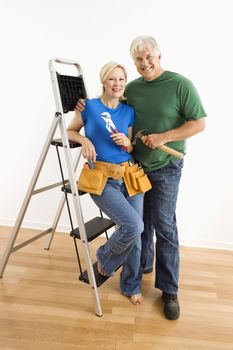 Middle-aged couple with household tools next to ladder.