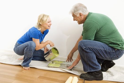 Middle-aged couple pouring paint into tray on drop cloth.