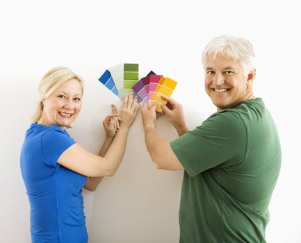 Middle-aged couple holding up and comparing paint swatches.