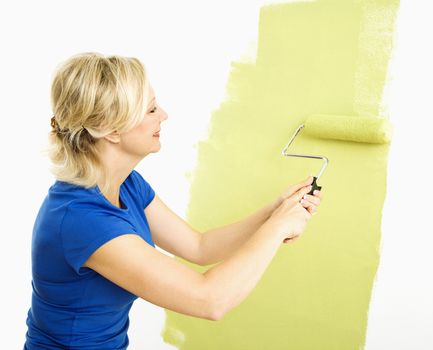 Middle-aged woman painting wall green with paint roller.