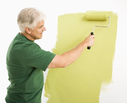 Middle-aged man painting wall green with paint roller.
