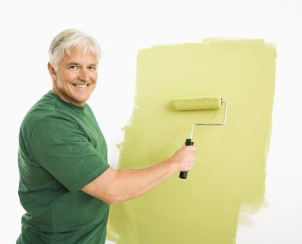 Middle-aged man painting wall green with paint roller smiling at viewer.