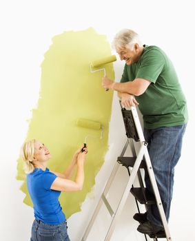 Middle-aged couple painting wall green with male on ladder.