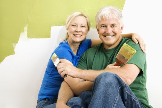 Middle-aged couple snuggling in front of wall they are painting green.