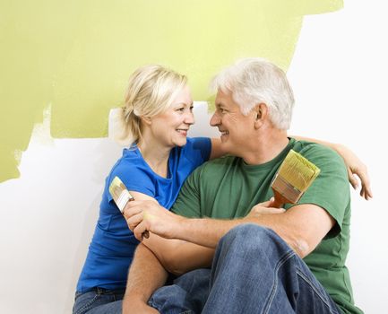 Middle-aged couple snuggling in front of wall they are painting green.