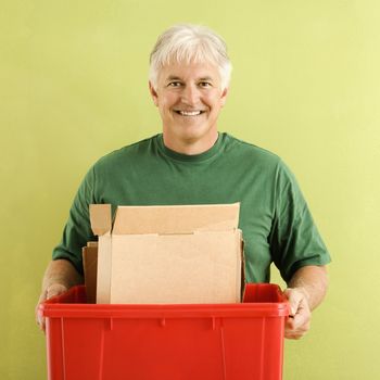 Portrait of smiling adult man holding recycling bin full of cardboard.