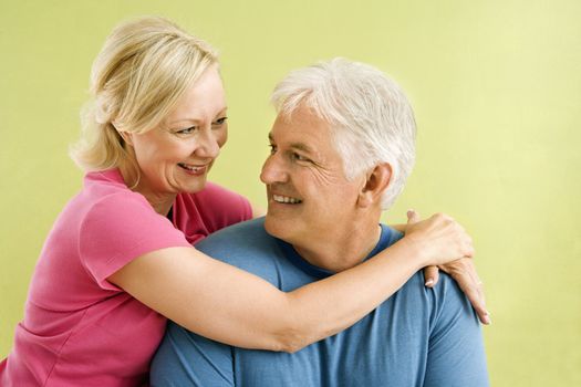 Portrait of smiling middle-aged couple in front of green wall hugging.