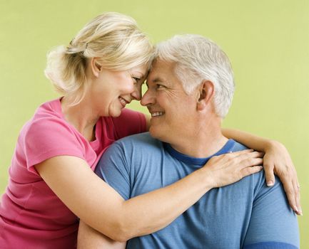 Portrait of smiling middle-aged couple in front of green wall snuggling.