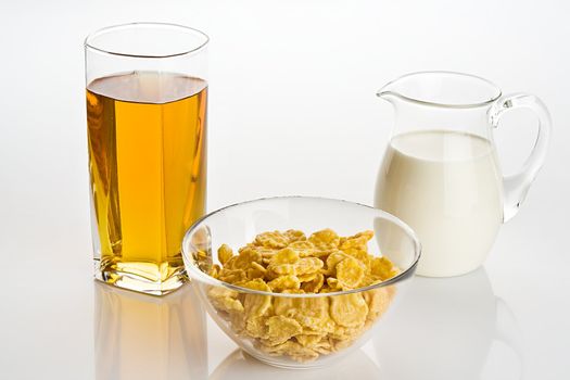 Big glass of apple juice, corn-flakes with milk in a transparent jug