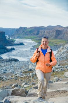 Cute woman hiking in the canyon Dettifoss waterfall in Vatnajokull National Park, Northeast Iceland. Vertical view