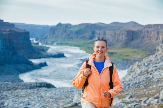 Cute woman hiking in the canyon Dettifoss waterfall in Vatnajokull National Park, Northeast Iceland.