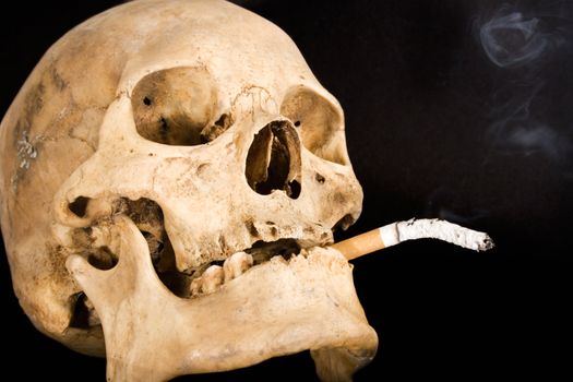 Human skull with burning cigarette. Isolated on a black background.