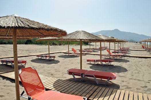 Rows of straw umbrellas and loungers at sandy beach Kalamaki Zakynthos, Greece.