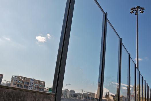 Distorted cityscape reflected on stained surface of highway traffic noise barrier.