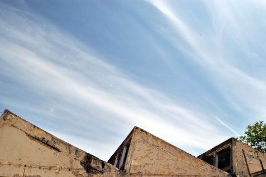 Partially demolished abandoned factory exterior and cloudy sky.
