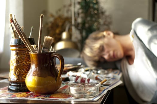 An artist sleeping on the table full of painting accessories.