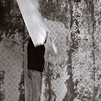 Obscured figure in empty room with torn wallpaper. Motion blur, black and white.
