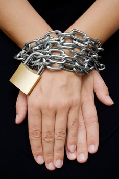 Female hands bound with chain and padlock. Isolated on a black background.