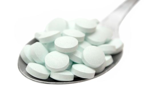 Greenish tablets on a silver spoon. Isolated on a white background.