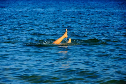 Suntanned legs of the young girl who has dived during time of bathing in the sea