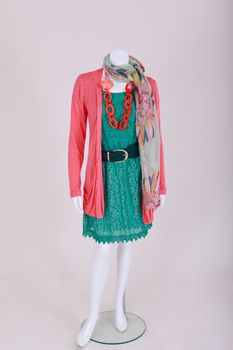 Mannequin dressed with a green dress with belt, pink jacket, chain and a cloth