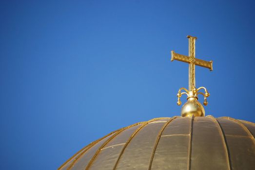 Golden orthodox cross and dome close-up on blue-sky background