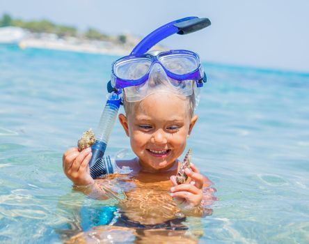 Portrait of young boy with seashells in snorkling equipment swimming in the transparent sea