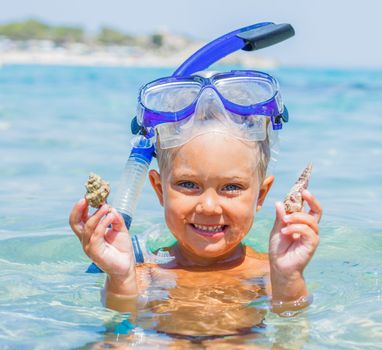 Portrait of young boy with seashells in snorkling equipment swimming in the transparent sea