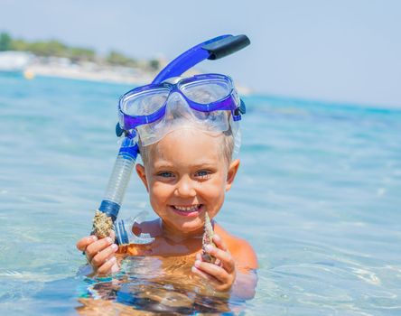 Portrait of young boy with seashells in snorkling equipment swimming in the transparent sea