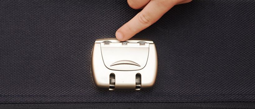 closeup photo of a combination lock on a black suitcase with child hand