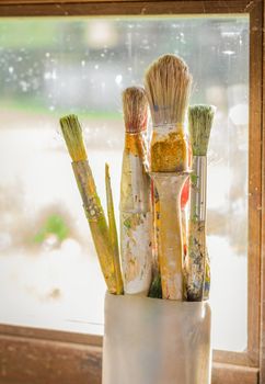 Set of paint brushes on jar, in front of a window
