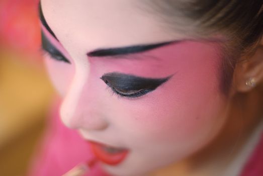 a chinese opera actress is painting her face at backstage.