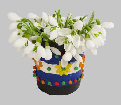 Bouquet of snowdrops in the decorative plasticine vase. Isolated on a light gray background.