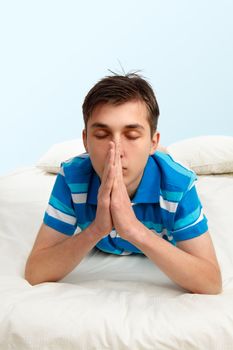 Teenage boy lying casually on bed nd praying.