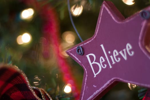 red star shaped believe ornament hanging on christmas tree