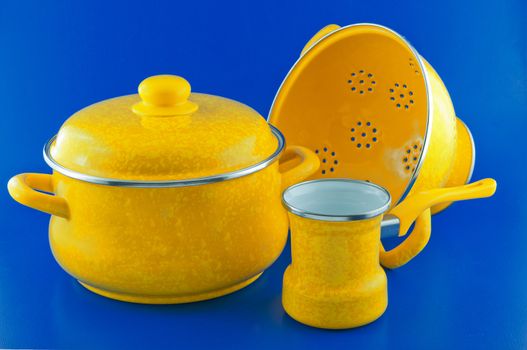 Kitchen utensils, pots Yellow, colander and a ladle against a blue background