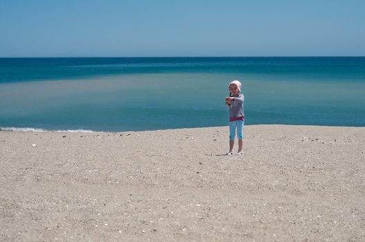 Small girl playing on the beach, blue sea