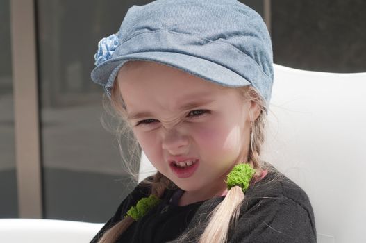 Grimacing little girl in jeans peaky cap