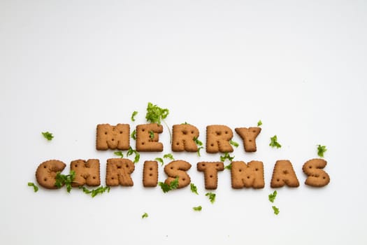 Merry Christmas wording from brown biscuits with green leaves on white background in landscape orientation
