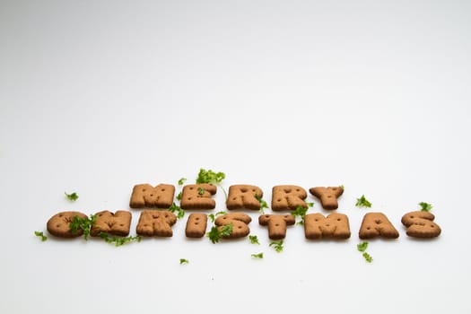 Merry Christmas wording from brown biscuits with green leaves on white background in landscape orientation