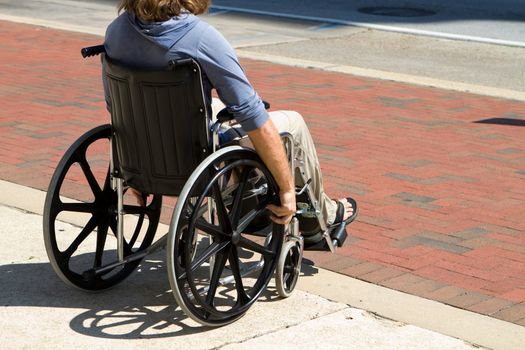 Injured male veteran sitting in his wheelchair rolls on the sidewalk.