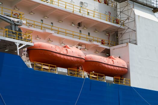 Orange survival lifeboats sit on the deck of an industrial ship.