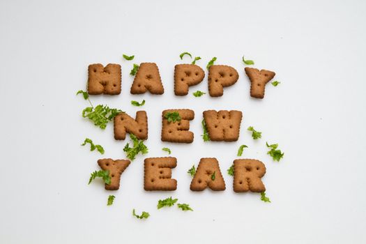 Happy New Year greeting words made by brown biscuits with green leaves on white surface in landscape orientation for background use