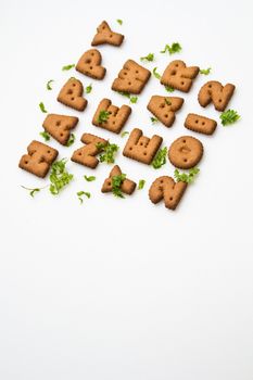 Angled view of Happy New Year greeting words made by brown biscuits with green leaves and copy space on upper center of white surface in portrait orientation for background use