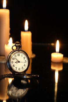 Pocket watch near lighting candles on dark background