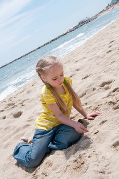 Little girl in jeans sitting on the beach